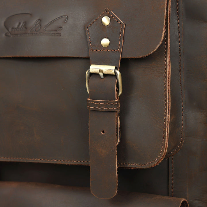Close-up of a brown leather bag with a strap and buckle, featuring a brand logo.