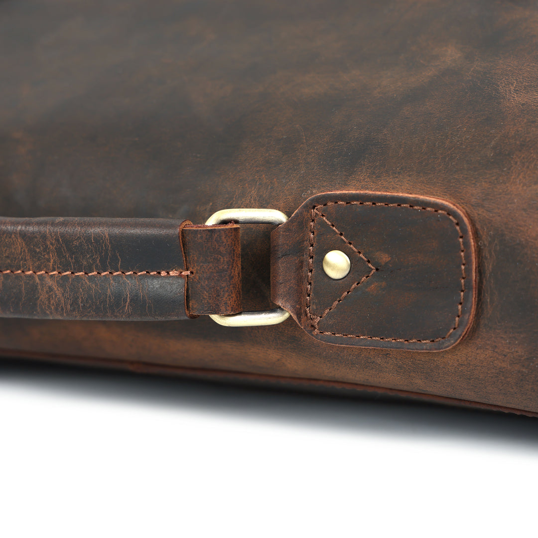 Close-up of a brown leather bag with a strap and metal buckle on a white background