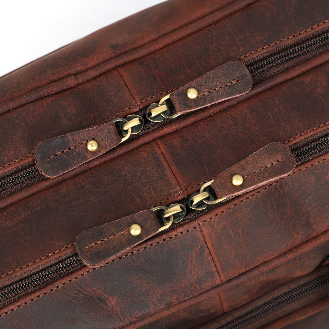 Close-up of a brown leather bag with gold zipper pulls on a white background