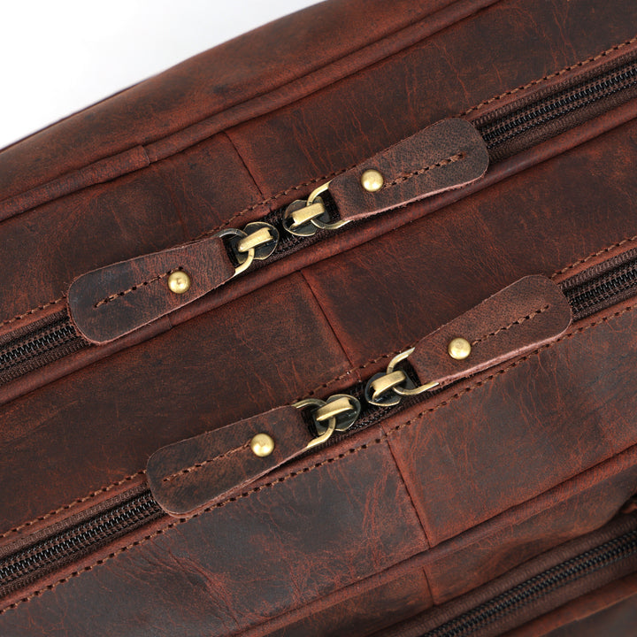 Close-up of a brown leather bag with gold zipper pulls on a white background