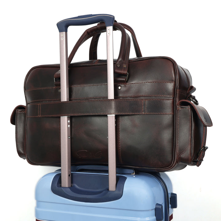 Brown leather duffel bag with extended handle on top of a blue suitcase.