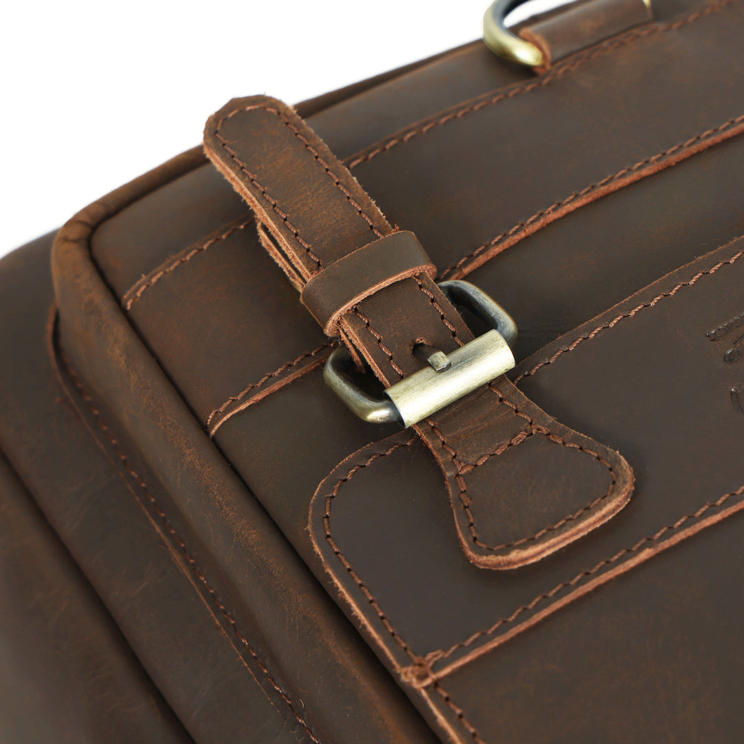 Close-up of a brown leather bag with a strap and buckle.