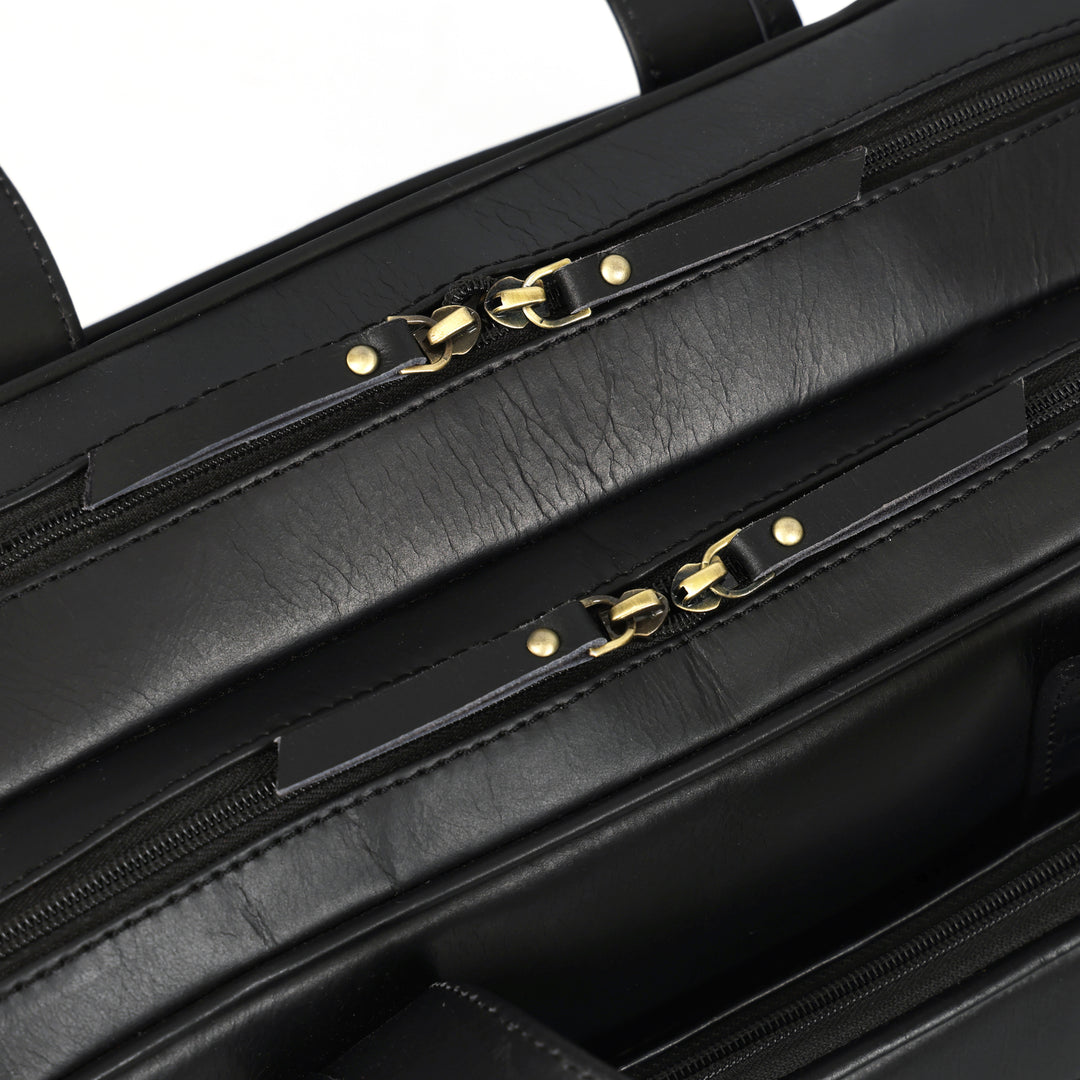 Close-up of a black leather briefcase with gold zipper pulls on a white background