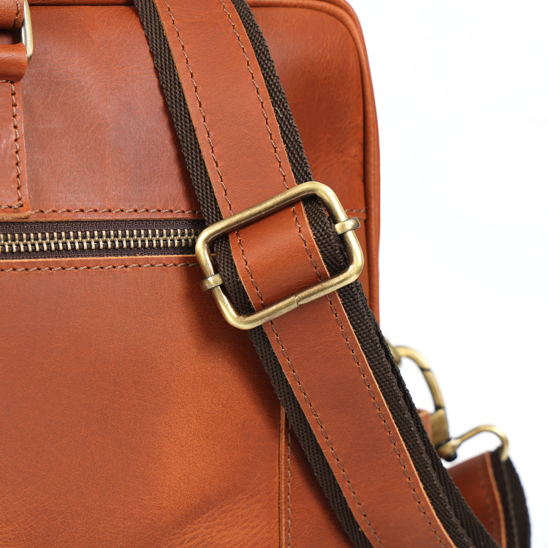 Close-up of a brown leather bag with a gold buckle and strap.