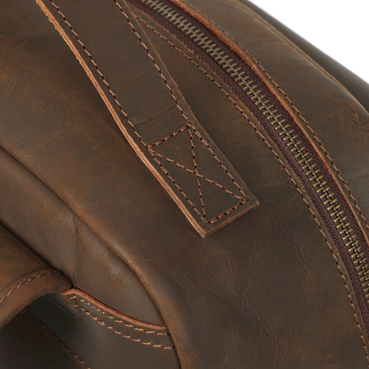 Close-up of a brown leather bag with a zipper and stitching detail.