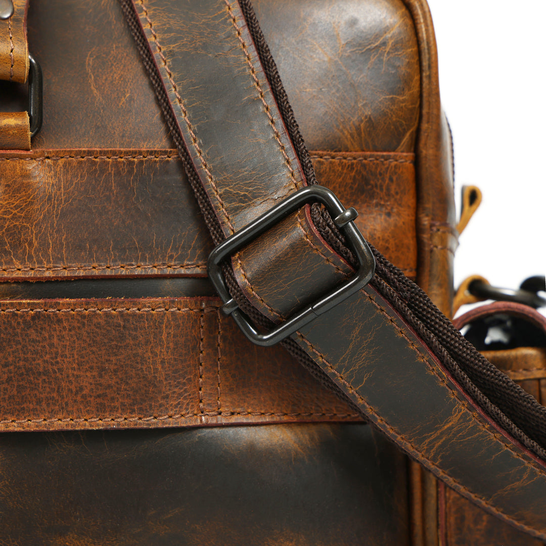 Close-up of a brown leather bag with a strap and buckle.