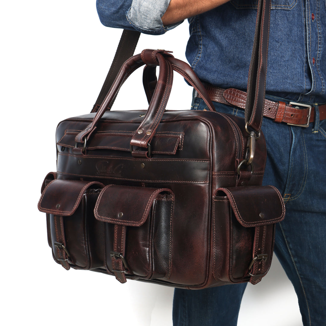 Brown leather briefcase held by a person wearing blue jeans and a brown belt.
