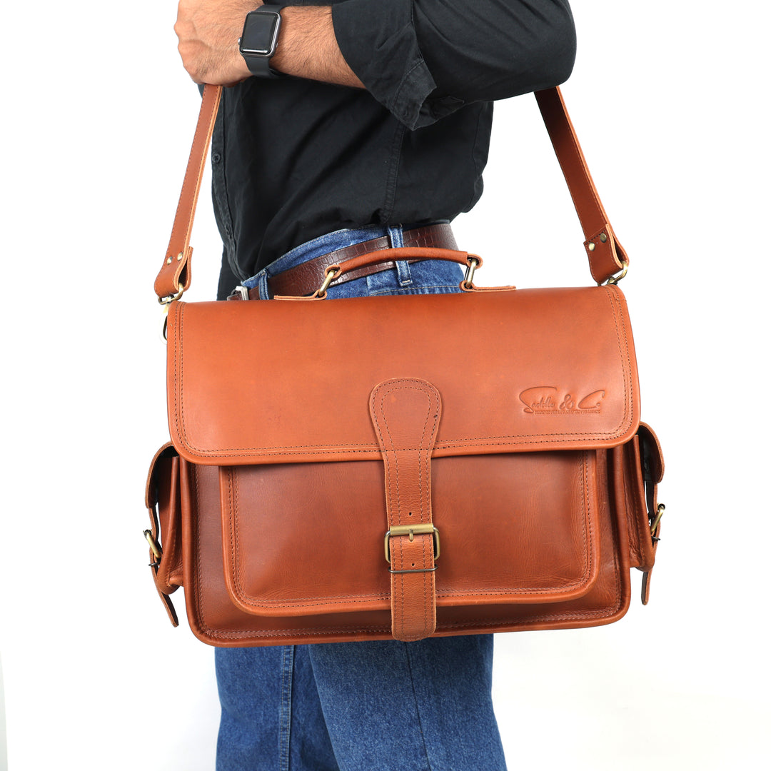Brown leather satchel bag worn by a person on a white background