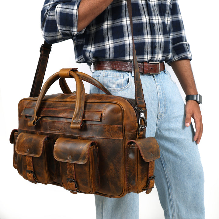 Brown leather briefcase carried by a person wearing a plaid shirt and jeans.