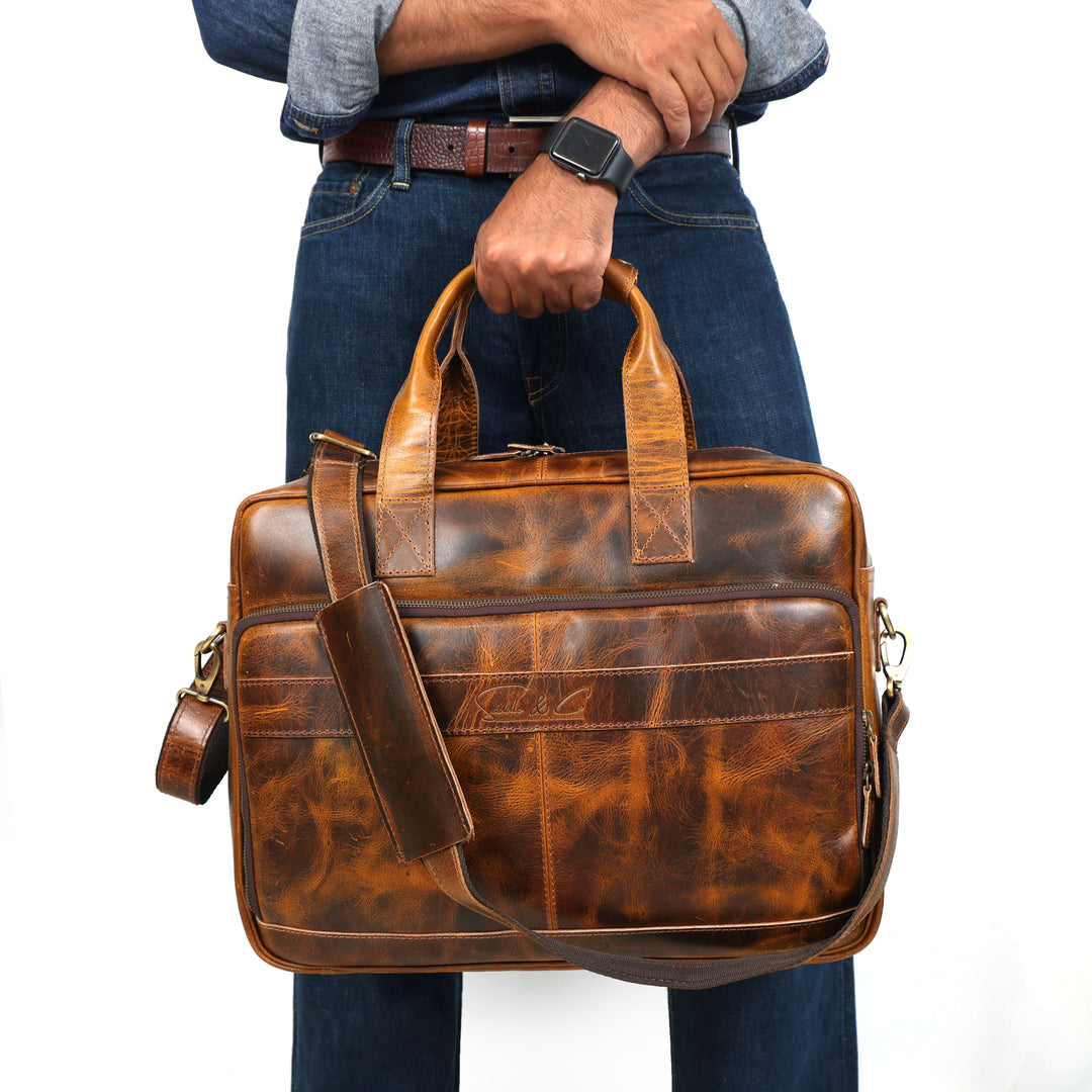 Brown leather briefcase held by a person wearing jeans and a shirt.