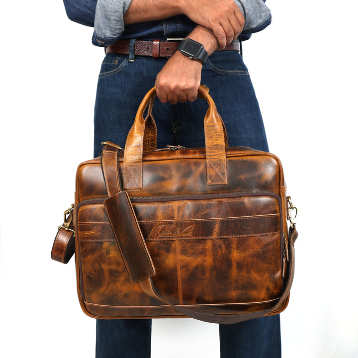Brown leather briefcase held by a person wearing jeans and a shirt.