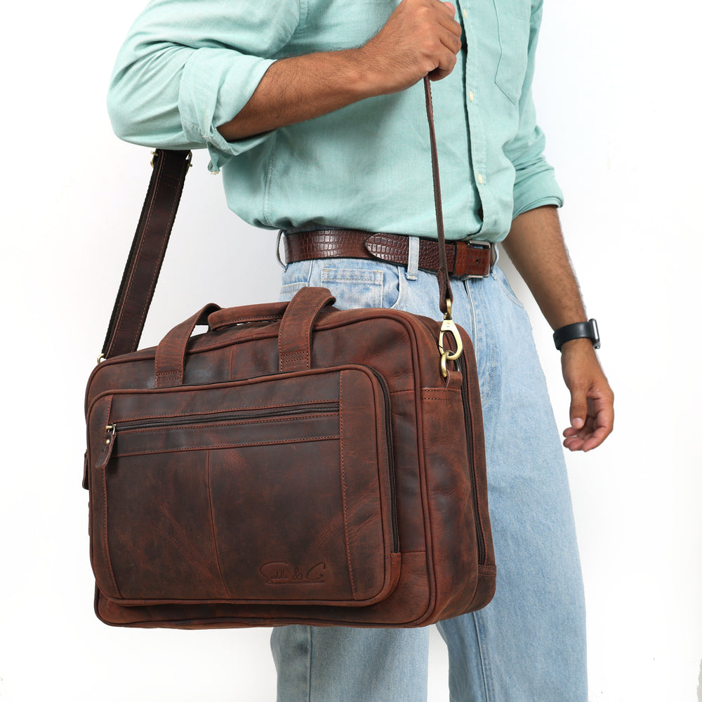 Brown leather briefcase carried by a person wearing a light blue shirt and jeans.