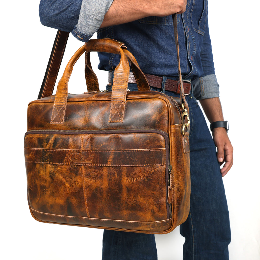 Brown leather briefcase held by a person wearing jeans and a denim jacket.