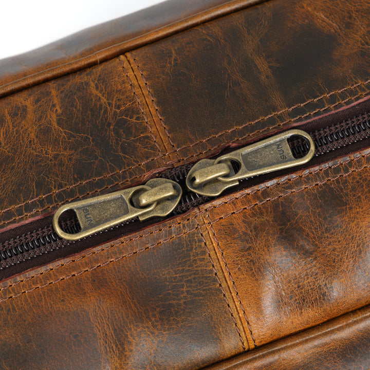 Close-up of a brown leather bag with brass zippers
