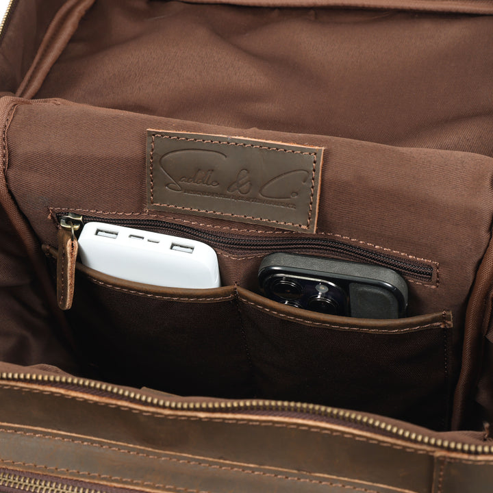 Brown leather bag with a visible brand label and electronic devices inside.